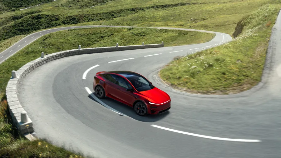 Red Tesla Model Y electric SUV driving through a mountain hairpin bend