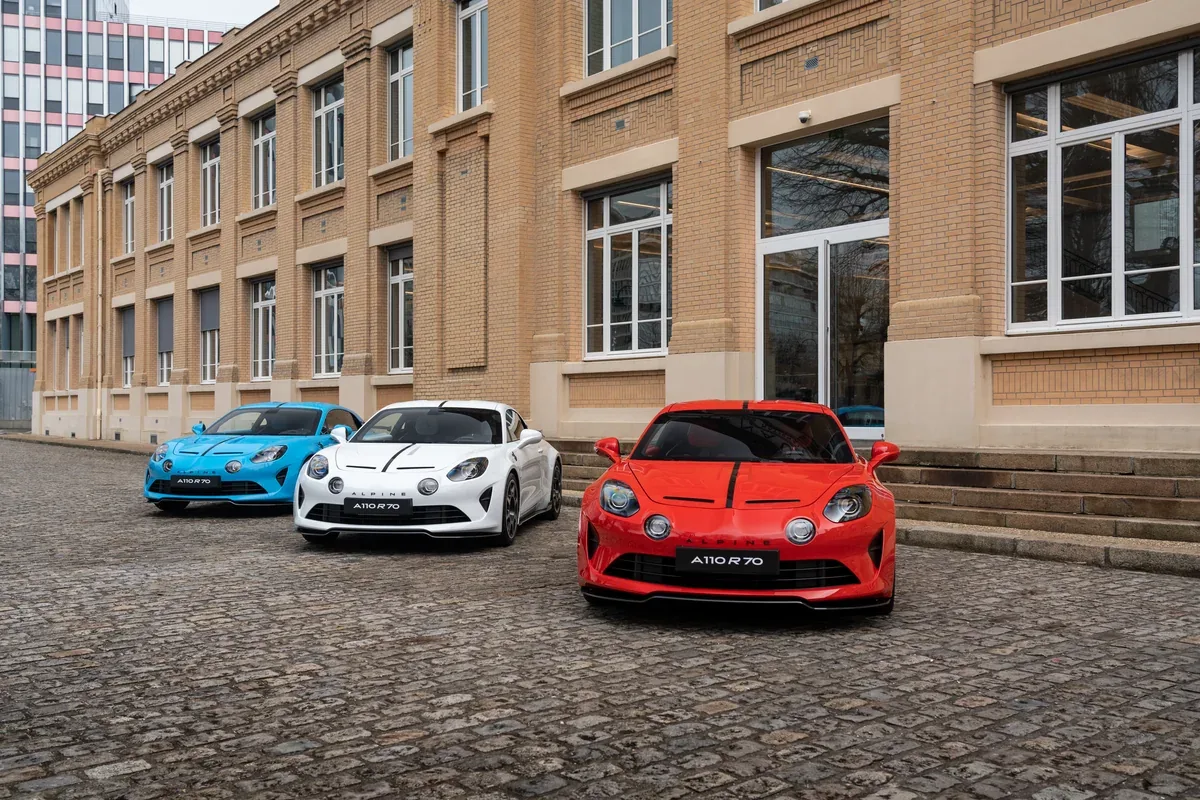 Three Alpine A110 R70 sports cars in blue, white and red outside a factory