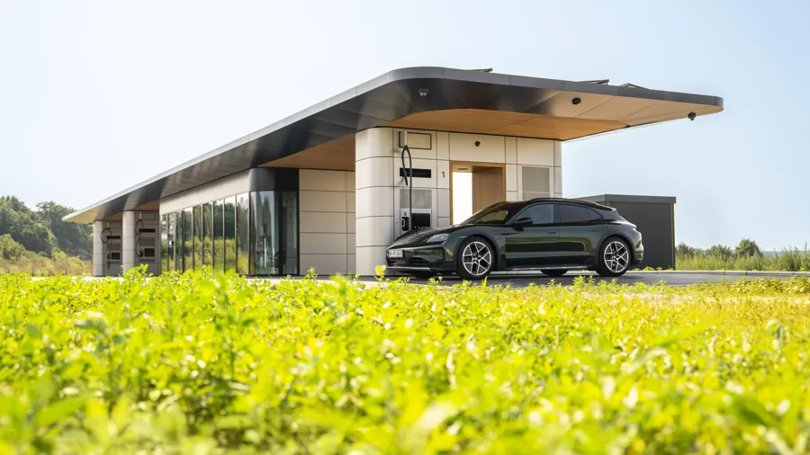 Dark green Porsche Taycan estate parked beside a Porsche charging station, side view