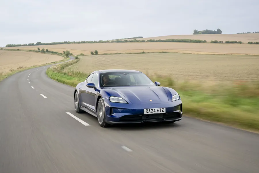 Porsche Taycan saloon in blue, front three-quarter view, driving on a country road