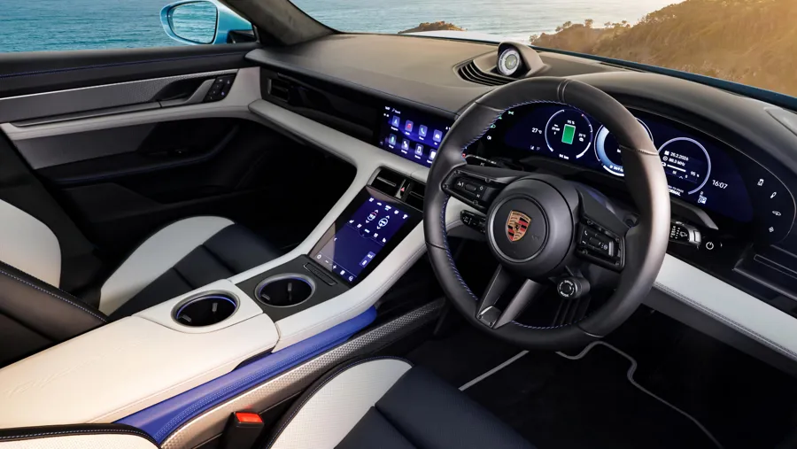 Porsche Taycan interior, right-hand drive, in cream and black leather with blue accents, showing the curved driver display and centre touchscreen
