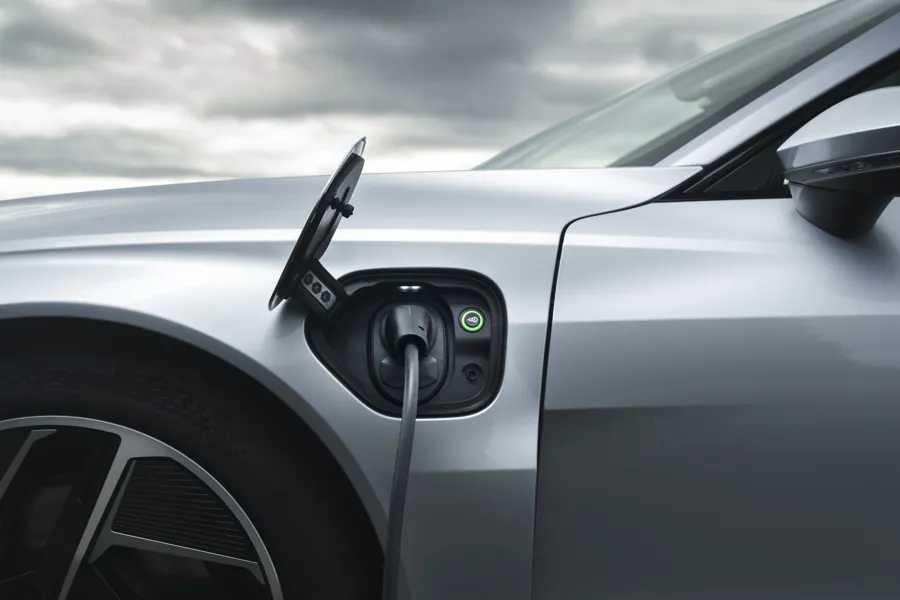 Silver Audi e-tron GT plugged in to charge, charging cable connected and status ring lit green